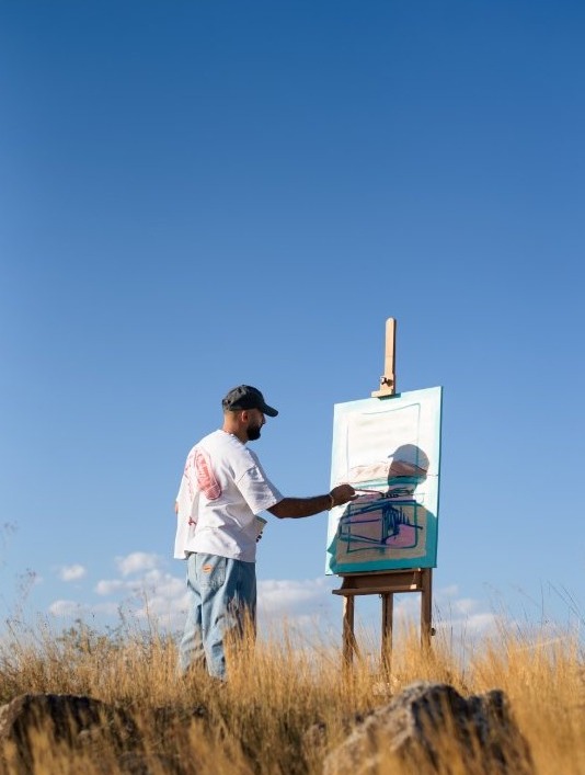 Gareggin painting at an easel under a clear blue sky in the dry golden hills