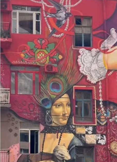 A large mural on a red residential building in central Yerevan reinterpreting Lady with an Ermine with Armenian ornaments, lace and doves