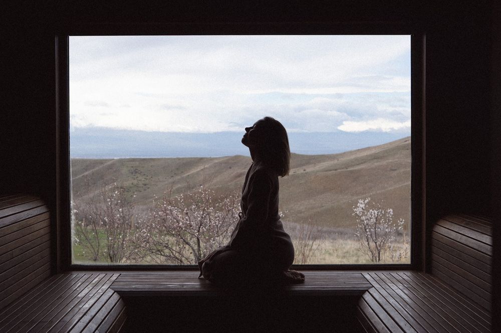 A figure resting by a window at Hoja Place with a view of the hills