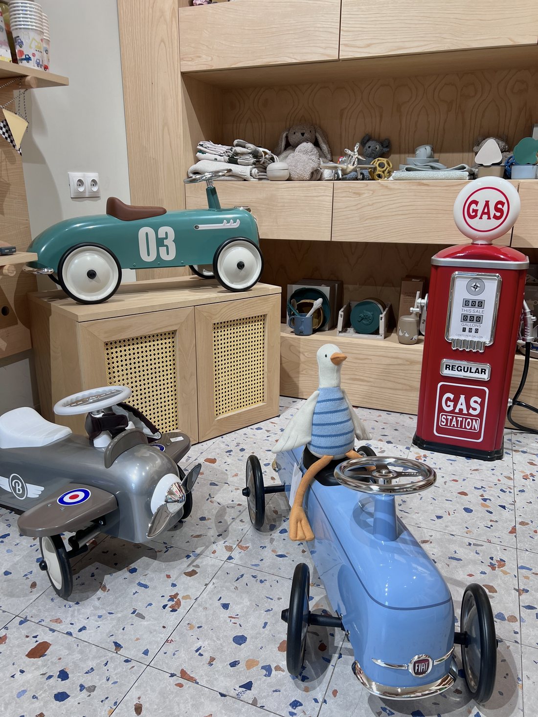 Inside the Memi Kids Corner shop: vintage metal ride-on cars, a toy gas pump and shelves of soft toys