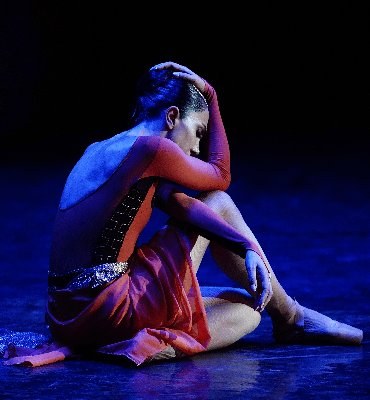A ballet dancer resting on stage under blue light at the Opera House