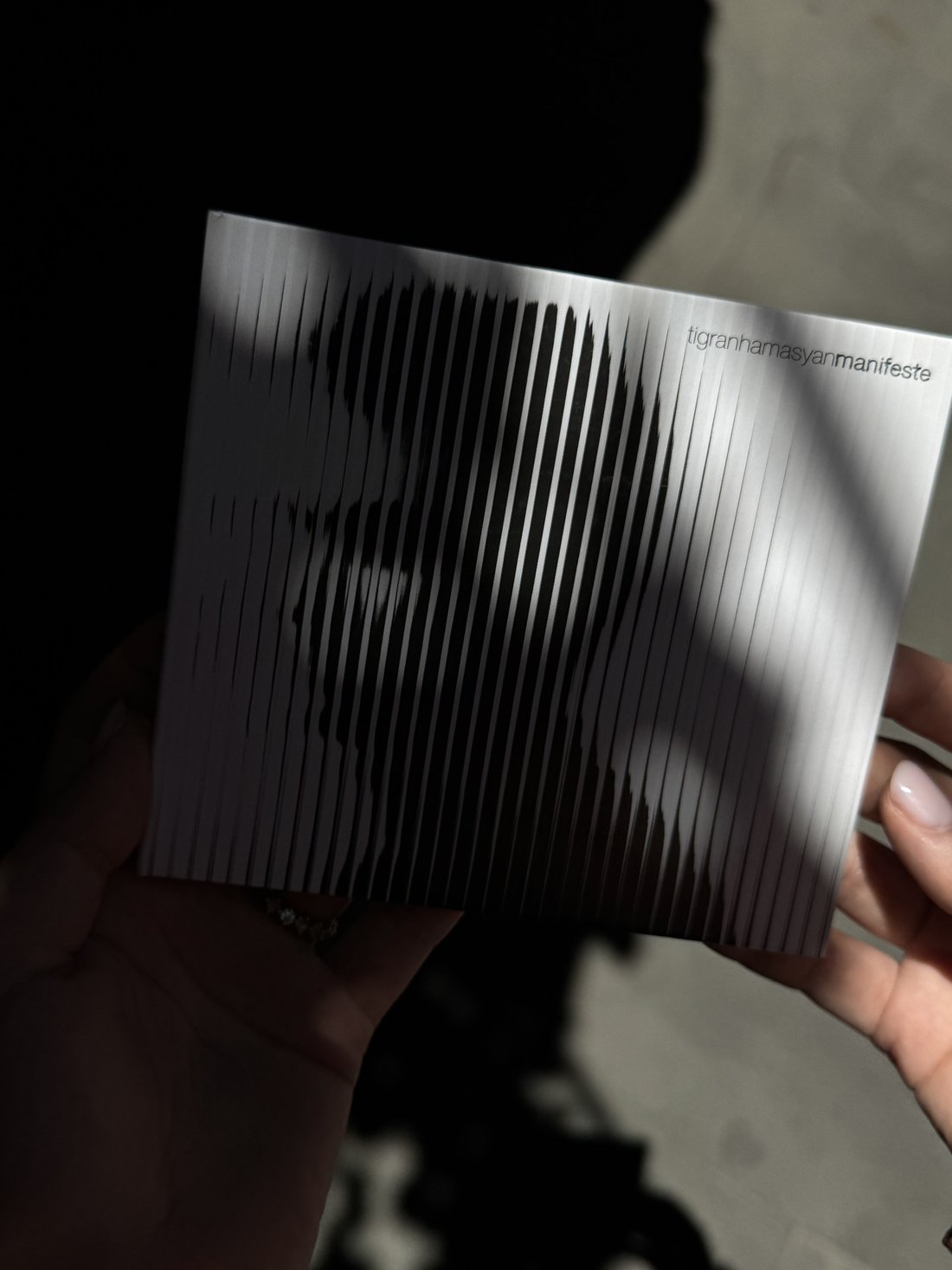 Tigran Hamasyan's Manifeste album held in hand, its silver striped cover catching the light